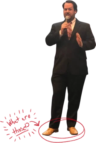 Wesley Harris speaking into a microphone wearing a black suit with tan shoes. The shoes have been circled in red; next to this is the handwritten text, 